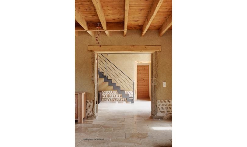 Vue de la pièce de vie avec enduits terre, planchers bois et escalier métallique