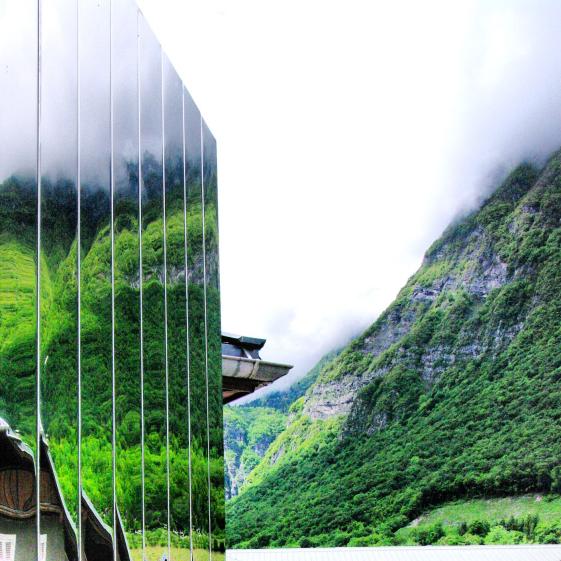 Photo de la façade miroir reflétant le massif des Bauges depuis la passerelle.  