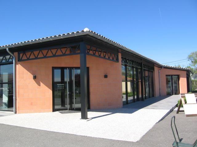 Vue de l'entrée avec parement briquettes, poteaux et structure métallique noirs.