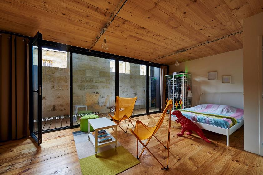 Une chambre lumineuse et son balcon derrière la façade existante
