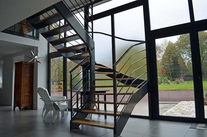 L'escalier de métal et de bois habite l'espace en transparence discrète derrière