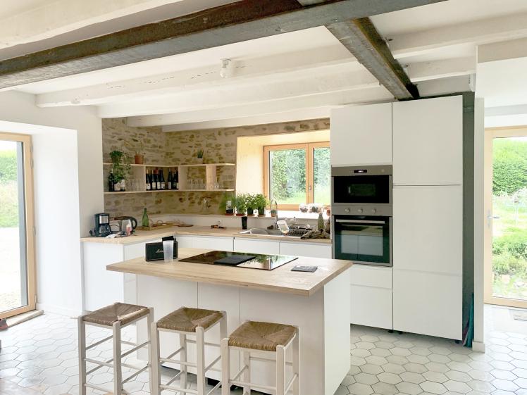 Vue sur la cuisine contemporaine blanche et chaleureuse grâce au mur pierres