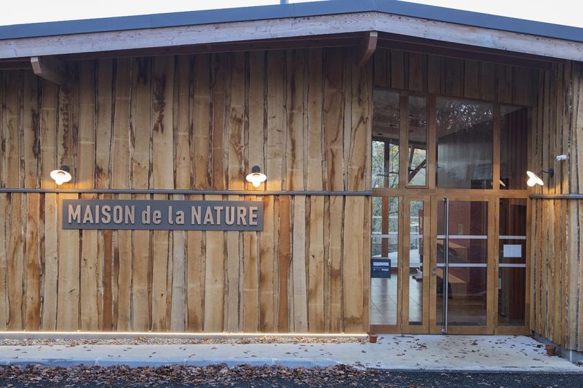 vue entrée du bâtiment -toiture à deux pans simples laissant lire la matière du batiment Maison de la nature, notamment le bardage bois chaitaignier en pose verticale brut non déligné.