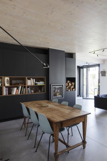Un grand meuble noir intègre bibliothèque, poêle et placard dans la zone de la salle à manger. Il rappelle la cuisine visible depuis le salon en suivant.