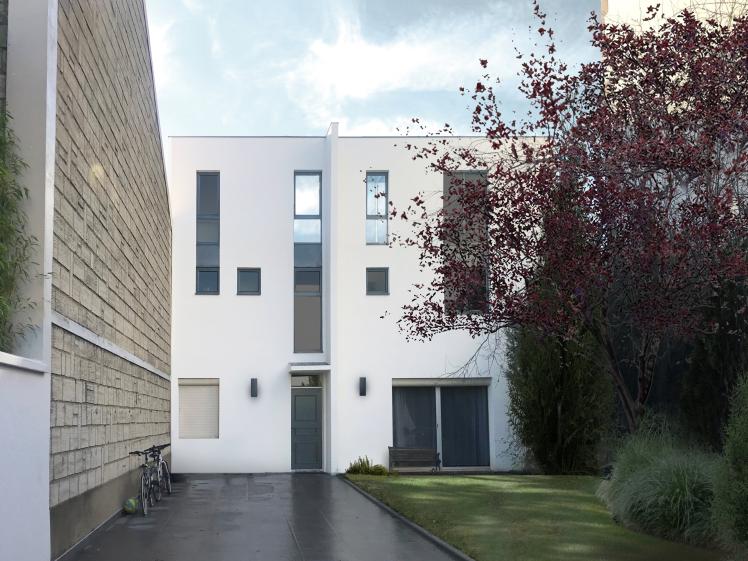Cette image montre une maison moderne à façade blanche avec des fenêtres étroites et verticales. L'entrée dispose d'une porte gris foncé entourée de luminaires muraux. À gauche, un mur en béton texturé borde une allée où sont garés des vélos. À droite, un jardin bien entretenu avec un arbre aux feuilles rouges apporte une touche naturelle. L'ensemble dégage une atmosphère minimaliste et épurée.