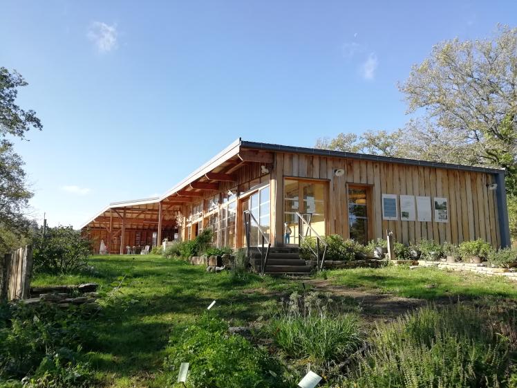 Vue du bâtiment depuis le jardin de culture - toiture à deux pans simples laissant lire la matière du batiment, notamment le bardage bois chaitaignier en pose verticale brut non déligné.