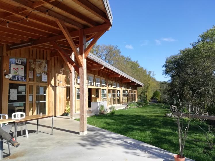 Vue du batiment sous l'auvent, autour du poteau princiapl de structure offrant un dessin arborescent, vue vers la serre solaire
