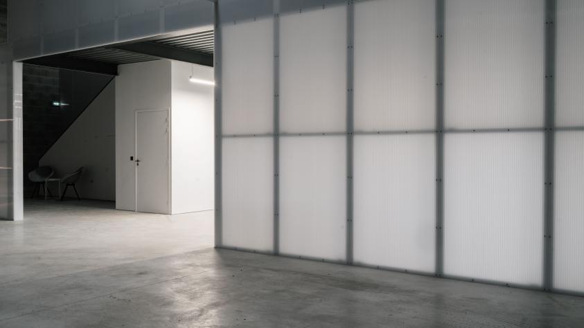 Bureau aux murs légers en polycarbonate translucide, éclairé par des néons diffusant une lumière douce et homogène.
