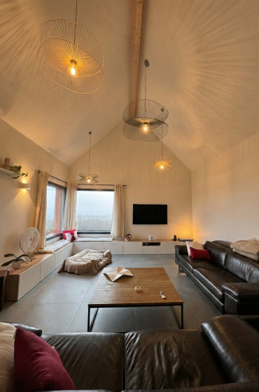 Le séjour bénéficie d’un volume généreux sous plafond, structuré par un aménagement sur mesure intégrant rangements bas et assises. La lumière naturelle, les vues lointaines et un éclairage travaillé composent un espace de vie à la fois convivial, confortable et ouvert sur le paysage.