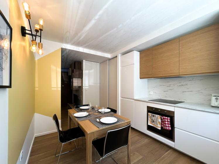 Cuisine linéaire équipée avec plan de travail effet marbre, rangements bois et blancs, table à manger pour quatre personnes dans un appartement en colocation