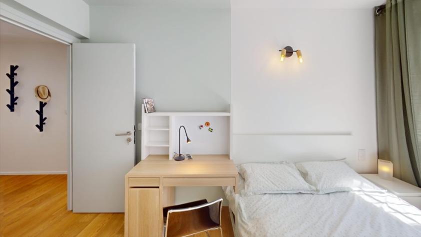 Chambre lumineuse avec lit double, bureau intégré avec étagères, lampe de travail et rangements, adaptée à une colocation