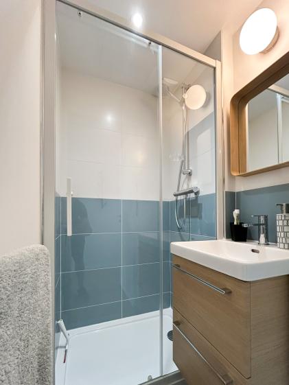 Douche vitrée avec carrelage bicolore, meuble vasque suspendu et éclairage mural, dans un appartement rénové