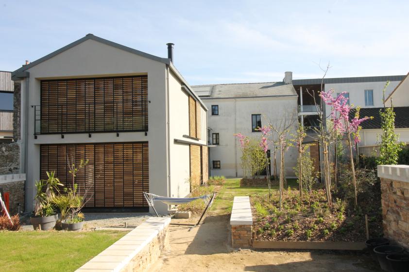 vue de l'extension fermée par les volets bois coulissants comme une grange et de la maison existante en fond de jardin.