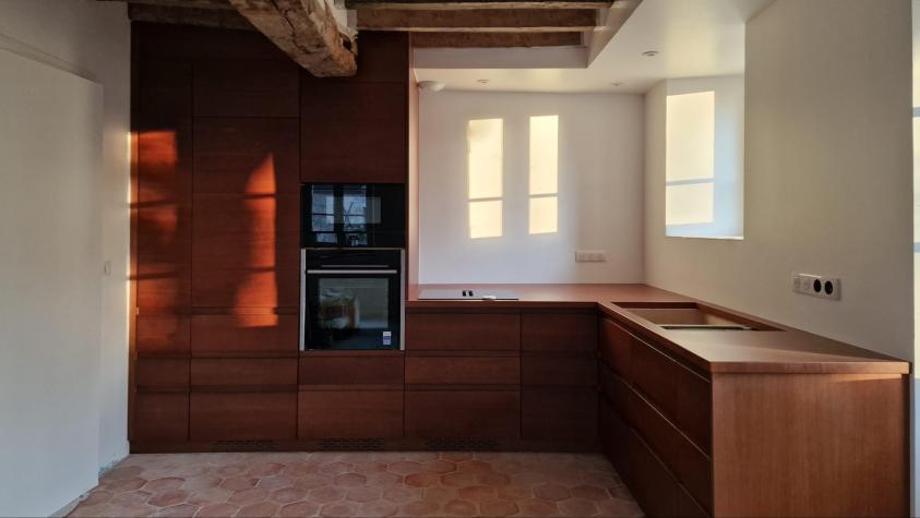 Photo d'une cuisine dans un subtil mélange traditionnel et contemporain, tomette artisanale au sol, boiseries en noyer sur fond de poutres apparentes taillées à l'herminette