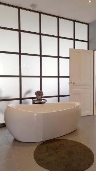 Salle de bain avec verrière et baignoire îlot Une salle de bain épurée structurée par une verrière sur mesure, apportant lumière et profondeur à l’espace.