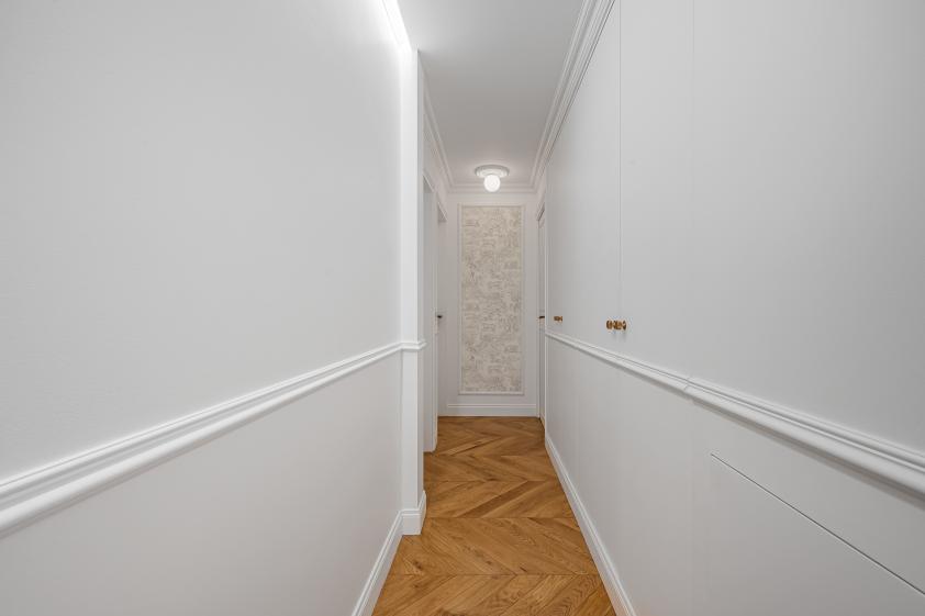 Couloir – Boiseries et détails haussmanniens Couloir rénové d’un appartement haussmannien à Saint-Germain-en-Laye, avec boiseries blanches, moulures et parquet en bois.
