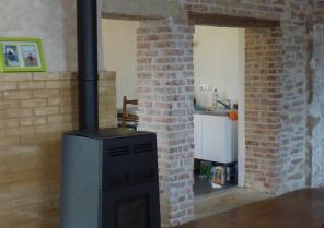 Le poele à granulés adossé à un mur de brique de terre cru chauffe la maison