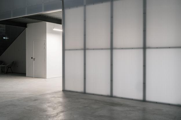Bureau aux murs légers en polycarbonate translucide, éclairé par des néons diffusant une lumière douce et homogène.