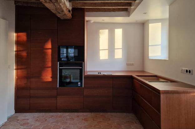 Photo d'une cuisine dans un subtil mélange traditionnel et contemporain, tomette artisanale au sol, boiseries en noyer sur fond de poutres apparentes taillées à l'herminette