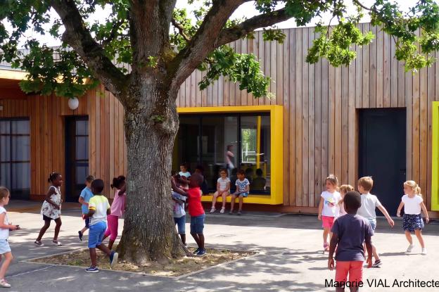 Une des cours du centre de loisir : Construction contemporaine à ossature bois avec de grands cadres de fenêtre colorés et débordants servant de bancs pour les enfants.