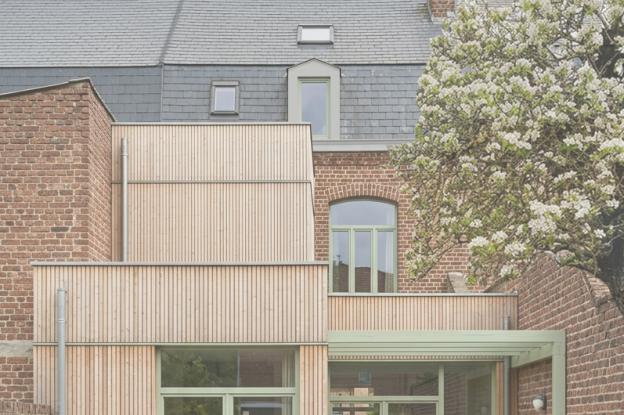 Façade arrière en brique d'une maison ancienne, étendue par des volumes contemporains en bardage bois clair et menuiseries vert clair ouvrant sur un jardin planté.