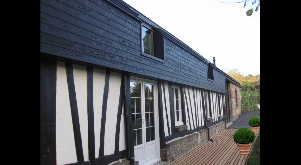 Une ossature bois revêtue d'un bardage bois de teinte noire a été utilisée pour modifier la toiture existante et permettre l'aménagement des combles de la longère.