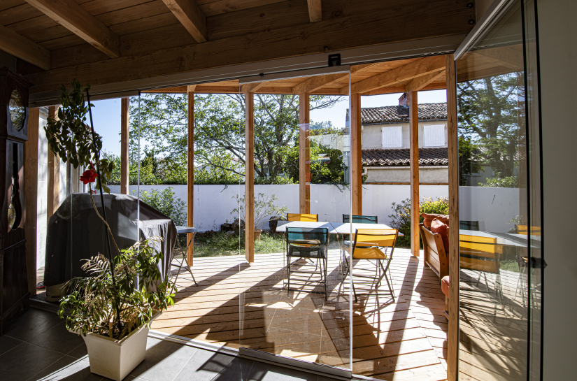 extension bois accueillant une entrée donnant sur une terrasse couverte, un salon d'extérieur. Contamin Bioley architectes